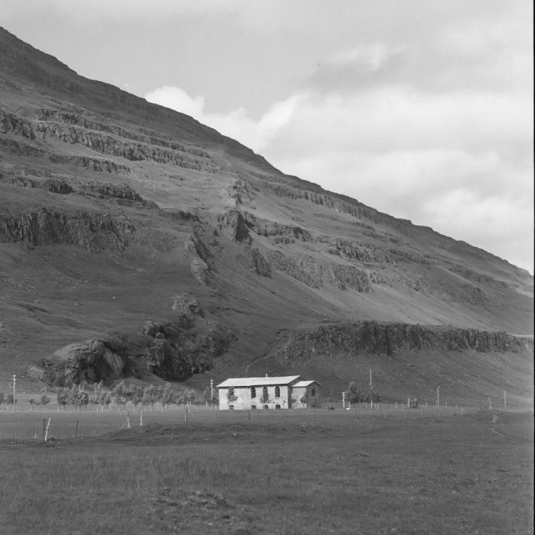 Ólafur Jónsson, ráðunautur og rithöfundur,  tók þessa mynd í Fljótsdal á Héraði, við kirkjustaðinn Valþjófsstað. Berggangurinn sem skásker Valþjófsstaðafjall kallast Tröllkonustígur og er mjög áberandi. Húsið á myndinni, Ungmennafélagshúsið, var byggt á árunum 1912 til 1917 af Ungmennafélagi Fljótsdæla og varð miðstöð alls félagsstarfs í sveitinni, skv. Fljótsdælu, bók Helga Hallgrímssonar náttúrufræðings um mannlíf og náttúrufar í Fljótsdalshreppi. Húsið var síðar rifið og nýtt byggt á sama stað um 1960. Það heitir Végarður er nú samkomuhús sveitarinnar.