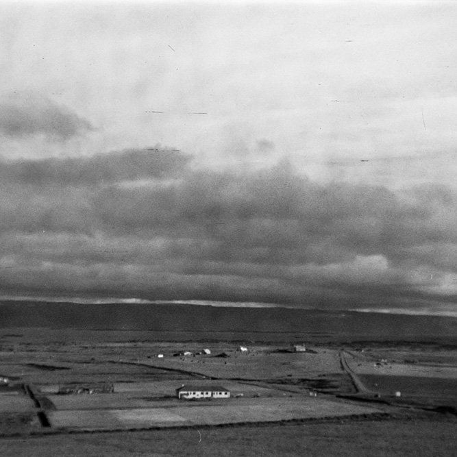 Ólafur Jónsson, ráðunautur og rithöfundur,  tók þessa mynd. Lesandi skrifar: Myndin er tekin af gamla þjóðveginum rétt austan við bæinn Grund, í áttina að Reykhólum. Hús tilraunastöðvarinnar næst. Kirkjan fjær til hægri. Sér yfir á Skarðsströnd. - Minjasafnið á Akureyri / a1-04071-31   frá Minjasafninu á Akureyri