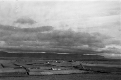Ólafur Jónsson, ráðunautur og rithöfundur,  tók þessa mynd. Lesandi skrifar: Myndin er tekin af gamla þjóðveginum rétt austan við bæinn Grund, í áttina að Reykhólum. Hús tilraunastöðvarinnar næst. Kirkjan fjær til hægri. Sér yfir á Skarðsströnd. - Minjasafnið á Akureyri / a1-04071-31   frá Minjasafninu á Akureyri