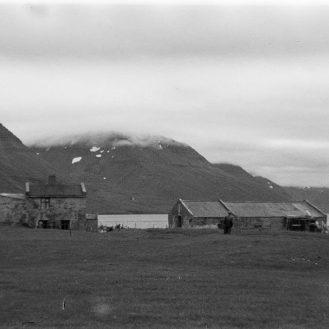 Þetta er Norðureyri við Súgandafjörð. Ólafur Jónsson ráðunautur og rithöfundur tók myndina, líklega laust eftir miðja síðustu öld og maðurinn fyrir miðri mynd Kristján Sigurðsson bóndi á bænum frá 1906 til 1949. Vert er að vekja athygli á steinfleyg – snjóflóðafleyg – vinstra megin á íbúðarhúsinu, sem er lengst til vinstri á myndinni. Hin húsin voru sögð í vari fyrir mögulegum snjóflóðum. Mynd sem tekin er á sama tíma birtist í bókinni Skriðuföll og snjóflóð eftir Ólaf Jónsson, 3. bindi (1992). - Minjasafnið á Akureyri / a1-04071-11 frá Minjasafninu á Akureyri