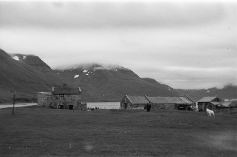 Þetta er Norðureyri við Súgandafjörð. Ólafur Jónsson ráðunautur og rithöfundur tók myndina, líklega laust eftir miðja síðustu öld og maðurinn fyrir miðri mynd Kristján Sigurðsson bóndi á bænum frá 1906 til 1949. Vert er að vekja athygli á steinfleyg – snjóflóðafleyg – vinstra megin á íbúðarhúsinu, sem er lengst til vinstri á myndinni. Hin húsin voru sögð í vari fyrir mögulegum snjóflóðum. Mynd sem tekin er á sama tíma birtist í bókinni Skriðuföll og snjóflóð eftir Ólaf Jónsson, 3. bindi (1992). - Minjasafnið á Akureyri / a1-04071-11 frá Minjasafninu á Akureyri