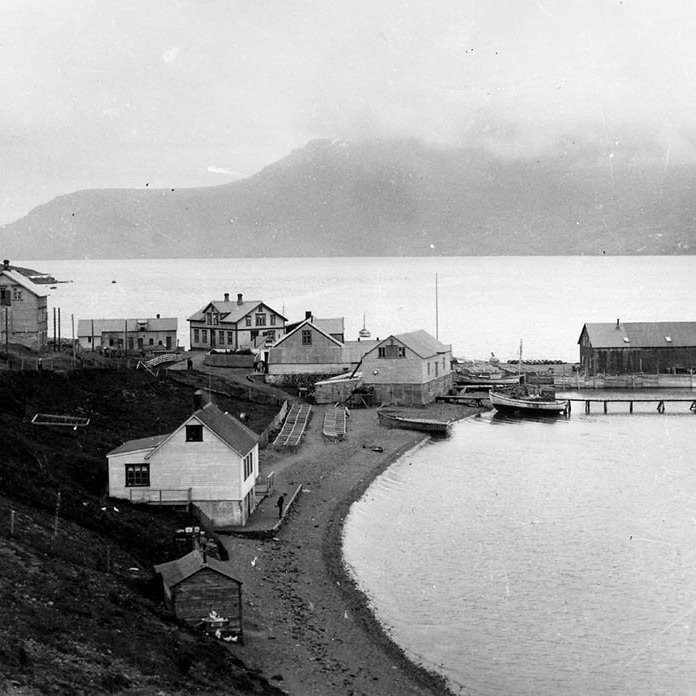 Ítarlegar upplýsingar hafa borist um þessa mynd: Þetta er Bakkagerðiseyri við Reyðarfjörð. Búðareyrin er litlu innar. Watnebræður byggðu þarna um eða rétt fyrir 1886. Bryggjan heitir Barkurinn og leifar hennar standa enn. Þeir munu hafa sökkt þarna barkskipi og byggt bryggjuna ofan á það. Næst fyrir ofan bryggjuna er pakkhús, sem nýtt var alveg fram yfir 1970. Þar fyrir ofan er annað pakkhús, líklega einnig nýtt sem sláturhús á tímabili. Þar fyrir ofan er hið eiginlega Wathnehús (snýr stafni í vestur með einn glugga) síðar nefnt Johansenshús eftir Rolf Johansen sem bjó þar og verzlaði. Næst kemur glæsilegt tveggja hæða íbúðarhús sem byggt var líklega 1918 (heitir Valhöll) úr efni úr öðru norsku húsi, Imslandshúsi sem stóð sunnan fjarðar. (Áður stóð á þessum stað íbúðarhús Watnebræðra sem þeir fluttu á Seyðisfjörð og varð þar eldi að bráð 1992) Síðan kemur steypt fjósbygging sem snýr norður suður. Efst er íbúðarhúsið Sunnuhvoll, byggt á þriðja áratugnum. Í fjörunni hér næst á myndinni er verzlunin Framsókn, síðast  í eigu Kristins Magnússonar (hann bjó í Sunnuhvoli). Áður höfðu verlzað þar Thuliníus, Hinar sameinuðu ísl. verzlanir og Magnús Magnússon. Handan fjarðar eru Breiðihjalli og Eyrafjall. Þar í fjallsegginni er drangur sem heitir EYRARMAÐUR.