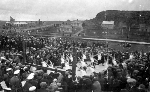 Hamarskotshamar í Hafnarfirði í fjarska. Ljósmyndarinn stendur á „skólamölinni“ við Barnaskóla Hafnarfjarðar, síðar Lækjarskóla, og leikfimiflokkurinn er á skólalóðinni. Gatan vinstra megin á myndinni er Öldugata. Langa húsið handan Öldugötu var oft kallað „bæjarbyggingin“. Lesandi, sem sendi upplýsingar, segir meðal annars: „Lengst til hægri á myndinni er hús sem mér sýnist vera með flatt þak og var að jafnaði kallað „kassahúsið“, einnig eftir að á það hafði verið sett venjulegt hallandi þak.“ Líklega er þetta Jónsmessuhátíð 29. júní 1924.  Minjasafnið á Akureyri / Mynd 29-358