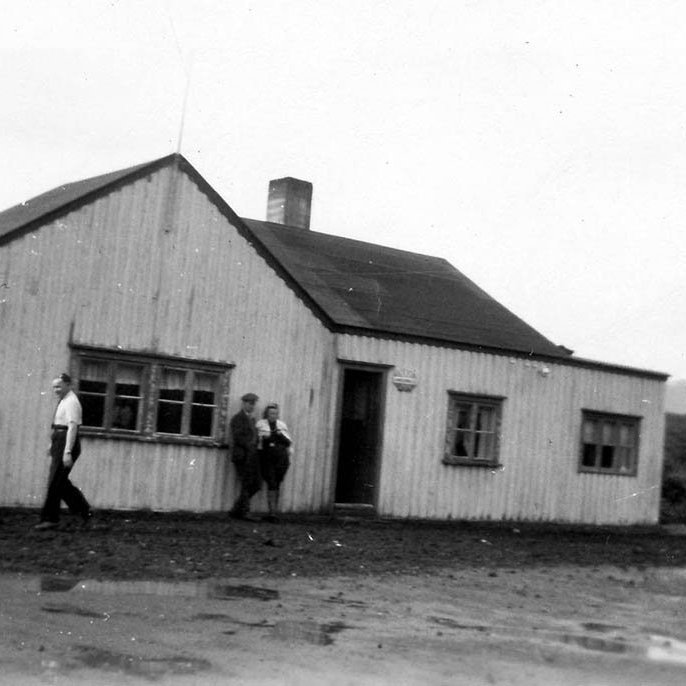 Gamli Hreðavatnsskálinn í Grábrókarhrauni, vertinn Vigfús Guðmundsson til vinstri.  Hægra megin við skálahornið sést í toppinn á Baulu og við hægri jaðar myndarinnar er dálítið horn af Grábrók. Myndin er frá upphafstímum ferðaþjónustu á Íslandi, segir í skeyti sem lesandi sendi. Annar segir: Þessi skáli stóð á steyptri plötu fyrir neðan Bifröst sem kom seinna. Húsið var flutt og er nú notað sem sumarbústaður fyrir neðan bæinn Hríshól. Sumarbústaðurinn heitir reyndar Hríshóll. / m-stae-1-7038 frá Minjasafninu á Akureyri