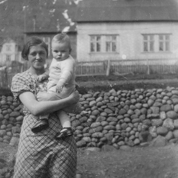 Myndin er tekin á Neskaupstað. Svæðið með áberandi dröngum í fjallsbrúninni heitir Drangaskarð. Enn hefur ekki tekist að grafa upp nöfn konu og barns en húsið í bakgrunni stendur við Miðstræti 1  - Minjasafnið á Akureyri / album-352-6 frá Minjasafninu á Akureyri