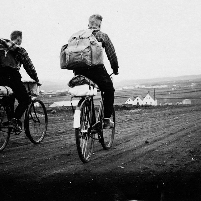 Bryndís Magnúsdóttir telur að hjólreiðamaðurinn til vinstri sé pabbi hennar, Magnús Ágústsson, og sá til hægri vinur hans, Haukur Árnason. Þeir hafi hjólað til Reykjavíkur á yngri árum, einmitt með tjald. Altjent hjóla mennirnir hér austur Miklubraut í Reykjavík og eru skammt austan við gatnamót við Háaleitisbraut. Úlfarsfell er til vinstri, Ártúnsbrekka og kartöflugeymslunar hægra megin í fjarska. Býlið Sjónarhóll, með þrjár burstir, stendur við Grensásveg og lengst til vinstri má sjá býlin Urðir og Hálogaland, efst á Sólheimahæð. Lesandi upplýsir að húsið Urðir  standi enn og sé í dag Sólheimar 36. Hálogaland brann í maí 1972 og var rifið í kjölfarið. - / m-stae1-16194 frá Minjasafninu á Akureyri