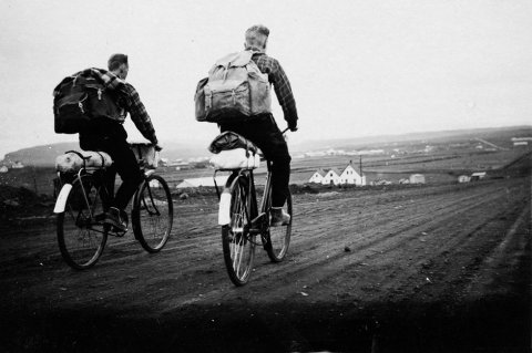 Bryndís Magnúsdóttir telur að hjólreiðamaðurinn til vinstri sé pabbi hennar, Magnús Ágústsson, og sá til hægri vinur hans, Haukur Árnason. Þeir hafi hjólað til Reykjavíkur á yngri árum, einmitt með tjald. Altjent hjóla mennirnir hér austur Miklubraut í Reykjavík og eru skammt austan við gatnamót við Háaleitisbraut. Úlfarsfell er til vinstri, Ártúnsbrekka og kartöflugeymslunar hægra megin í fjarska. Býlið Sjónarhóll, með þrjár burstir, stendur við Grensásveg og lengst til vinstri má sjá býlin Urðir og Hálogaland, efst á Sólheimahæð. Lesandi upplýsir að húsið Urðir  standi enn og sé í dag Sólheimar 36. Hálogaland brann í maí 1972 og var rifið í kjölfarið. - / m-stae1-16194 frá Minjasafninu á Akureyri