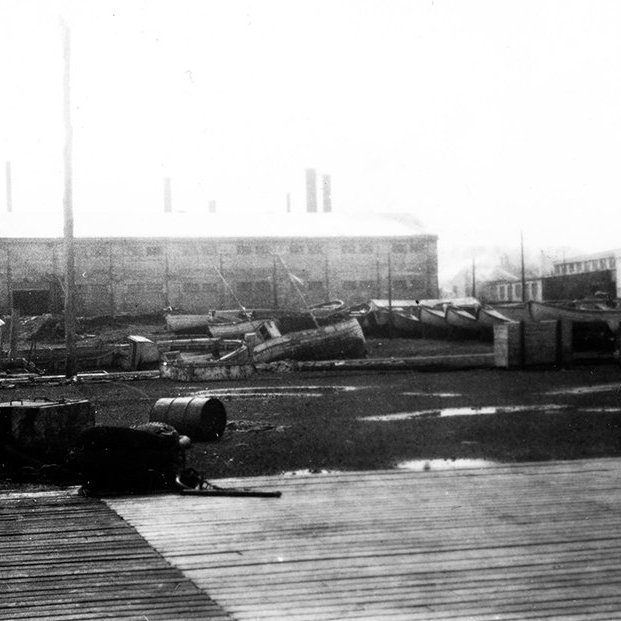 Myndin er frá Vestmannaeyjum. Lesandi sendi eftirfarandi: Þetta svæði var sunnan núverandi fiskimjölsverksmiðju Vinnslustöðvarinnar (VSV) (mjölhús á myndinni) og austan fiskvinnsluhúss Vinnslustöðvarinnar. Þarna standa núna fiskvinnsluhús Vinnslustöðvarinnar. - / m-stae1-16300 frá Minjasafninu á Akureyri