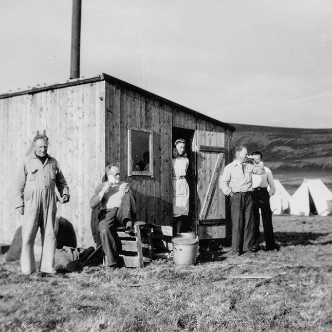 Talið er líklegt að á myndinni sé vegavinnuflokkur en hvorki hafa borist ágiskanir um hvaða fólk er á myndinni eða hvar hún er tekin. Lesandi sendi þó þessa bráðskemmtilegu lýsingu: „Þetta er augljóslega vegavinnuhópur og matarskúrinn í forgrunni en þar hafði ráðskonan lítið afþiljað herbergi. Tjöldin voru svo reist allt í kring og svona búðir voru á mörgum heiðarvegum um allt land. Greinilega helgarleyfi fram undan og karlarnir að raka sig og funsa sig fyrir heimferð yfir bláhelgina.“ - Þeir sem kunna að búa yfir upplýsingum um myndina eru hvattir til að senda þær á netföngin hg@minjasafnid.is og skapti@akureyri.net - / m-stae1-16483 frá Minjasafninu á Akureyri