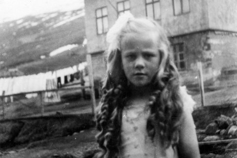 Stúlkan á myndinni heitir Kristbjörg Böðvarsdóttir, kölluð Krilla, fædd 1942. Hún býr nú á Reyðarfirði en myndin er tekin fyrir utan æskuheimili hennar, Valhöll á Eskifirði sem nú er Hólavegur 3. Einu sinni var þetta hús spítalinn á staðnum og móðir Kristbjargar oft nefnd Helga á spítalanum. Gaman er að segja frá því að systir Helgu, móður Kristbjargar, var Björg Finnbogadóttir, jafnan kölluð Bella, sem bjó í áratugi á Akureyri og er mörgum eftirminnileg.- / m-stae1-16436 frá Minjasafninu á Akureyri