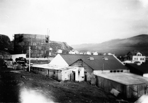 Þetta er á Skagaströnd. Myndin er tekin nálægt vestari enda Spákonufellshöfða nálægt svokölluðu Hólsnefi, skv. pósti frá Lárusi Ægi Guðmundssyni á Skagaströnd. Lengst til vinstri er lýsis- eða olíutankur fyrir síldarverksmiðju SR sem reist var á Skagaströnd á árunum 1943 – 1945, segir hann og á vef Héðins í Reykjavík kemur fram að um olíutank sé að ræða. Starfsmenn fyrirtækisins hafi lokið við að smíða tankinn árið 1947. Lárus Ægir segir: Byggingarnar neðst á myndinni eru nú allar horfnar en stóðu þar sem síðar var byggt frystihús en þar var jafnframt lítil bryggja sem byggð var ca. upp úr 1930. Sum íbúðarhúsanna sem sjást á myndinni eru enn á sínum stað en önnur eru horfin. - / m-stae1-15593 frá Minjasafninu á Akureyri