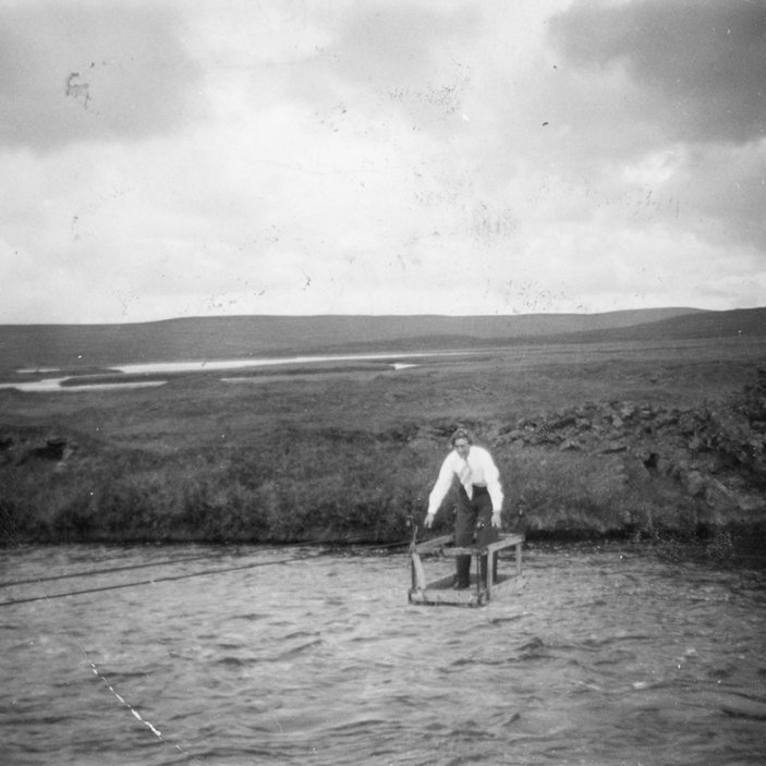 Konan er þarna í kláfi sem eitt sinn var yfir Laxá í Mývatnssveit við bæinn Helluvað. „Kláfurinn er rétt fyrir ofan þar sem gamli brúsapallurinn á Helluvaði var við veginn. Strengirnir eru enn á og stólpar hlaðnir með steinlími,“ sagði Mývetningurinn Benedikt Sigurðarson, fyrrverandi skólastjóri á Akureyri, í athugasemd eftir að myndinni var deilt á Facebook. - / m-stae1-16763 frá Minjasafninu á Akureyri