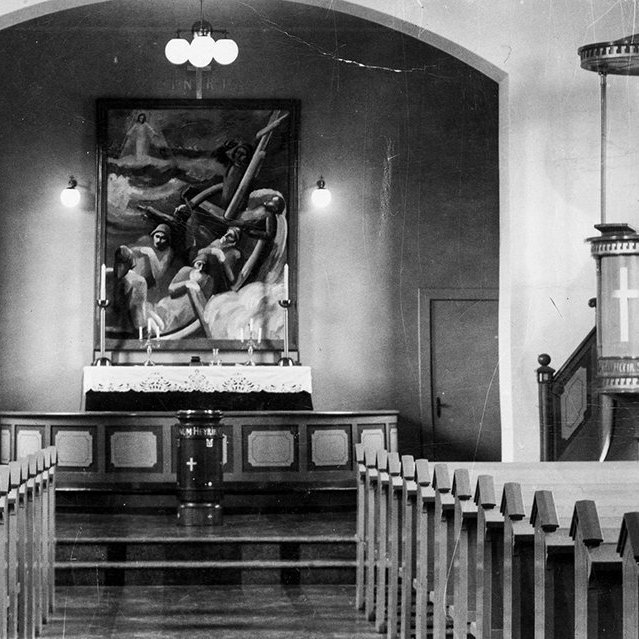 Þetta er Siglufjarðarkirkja. Altaristaflan er óvenjuleg en tilkomumikil, mesta prýði kirkjunnar að margra mati. Hún er máluð af Gunnlaugi Blöndal og var afhjúpuð 5. september 1937. - / m-stae1-17014 frá Minjasafninu á Akureyri