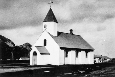 Þetta er Landakirkja í Vestmannaeyjum. Bygging kirkjunnar hófst árið 1774 og lauk 1778, og er hún þriðja elsta steinkirkja hér á landi, á eftir Viðeyjarkirkju og dómkirkjunni á Hólum. Lítil forkirkja (anddyri), sem sést á myndinni, var reist við vesturdyr kirkjunnar árið 1903 og á árunum 1955 til 1959 var byggð sú forkirkja og turn sem einkenna kirkjuna í dag. Myndin er því tekin einhvern tíma fyrir 1955. - / m-stae1-17071 frá Minjasafninu á Akureyri