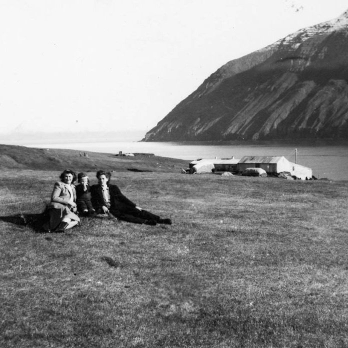 Myndin er tekin á hesthúsavellinum á Ytri-Á á Kleifum í Ólafsfirði. Í baksýn eru fjárhúsin á Ytri-Á og Múlinn. Fjárhúsin hafa breyst töluvert, helmingurinn af þeim hefur verið rifinn og hlutinn þar sem lægra þakið á myndinni er var hækkaður og settur hærri stafn og brattara þak.
Konurnar tvær eru sagðar dætur Finns Björnssonar og Mundínu Freydísar Þorláksdóttur sem eignuðust 20 börn saman og bjuggu á neðri hæðinni á Ytri-Á. Lesandi taldi að konurnar gætu verið Stefanía Gunnlaug og Birna en Laufey systir þeirra var einnig nefnd. Ekki er enn vitað hvaða barn er á milli þeirra. - / m-stae1-17478 frá Minjasafninu á Akureyri