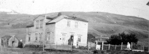 Þetta er gamli prestsbústaðurinn á Grenivík. Björn Ingólfsson, fyrrverandi skólastjóri á Grenivík, sendi fróðlegar og skemmtilegar upplýsingar, einu sinni sem oftar. Björn skrifar:
Húsið var byggt 1903 fyrir sóknarprestinn í Grenivík, séra Árna Jóhannesson. Hann bjó þar með stórri fjölskyldu til dauðadags 1927. Þá flutti í húsið Jóhann J. Kristjánsson læknir sem líka átti stóra fjölskyldu. Þau bjuggu þar til 1937 er þau fluttu til Ólafsfjarðar. Þá var húsið rifið og byggt nýtt læknishús. Símstöð var í húsinu frá 1919 til 1933.
Myndin er tekin eftir 1931 því að í kirkjugarðinum má sjá minnismerkið sem er á leiði sonar lækinshjónanna Hannesar Jóhannssonar (1926-1931). Líklega er þetta frú Inga Guðmundsdóttir sem stendur á pallinum - / m-stae1-17502 frá Minjasafninu á Akureyri