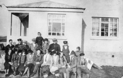 Myndin er tekin við Munkaþverá í Eyjafirði. Una Margrét Jónsdóttir, útvarpskona, skrifaði eftirfarandi: „Ég er nú búin að sýna Kristínu Jónsdóttur móður minni (Gígí) myndina. Það er rétt að hún er tekin á Munkaþverá sunnan undir húsveggnum. Samkvæmt áliti mömmu eru þessir á myndinni, talið frá vinstri. Aftari röð: Ingólfur Pálsson frá Uppsölum, óþekktur, Jónas Þorleifsson frá Grýtu (eða bróðir hans), svo Jónas Halldórsson frá Rifkelsstöðum. Drengurinn er líklega Jón Stefánsson á Munkaþverá, þá kemur óþekktur maður, svo Garðar Halldórsson frá Rifkelsstöðum og síðast Marinó Jónsson frá Uppsölum. (Fyrst var mamma reyndar á því að sá ysti til hægri væri Þorbjörn eða Sigurjón frá Borgarhóli, en hallaðist svo að því að það væri Marinó.) Þá kemur fremri röð frá vinstri: Líklega er Stefanía frá Steinsstöðum í Öxnadal yst t.v. þær næstu tvær álítur mamma að séu frænkur okkar, tvíburarnir Laufey og Sigríður Stefánsdætur, en er þó ekki alveg viss. Þá kemur Sigríður Halldórsdóttir frá Rifkelsstöðum, svo óþekktur maður og þrjár óþekktar konur, en ystur til hægri er, samkvæmt áliti mömmu, Valtýr Jónsson frá Borgarhóli. Allra fremst sjást höfuð tveggja ungra pilta og heldur mamma að sá sem er til vinstri geti verið Jóhann Rist. Þess skal líka getið að mömmu finnst líka koma til greina að stúlkan með flétturnar, þriðja frá hægri, sé Sigríður Stefánsdóttir, en þá getur hún náttúrlega ekki verið þriðja frá vinstri.“