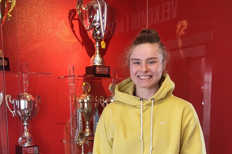 Maddie Sutton við bikaraskáp í Hamri. Að baki hennar, á efstu hillu, trónir bikarinn sem hún og liðs…